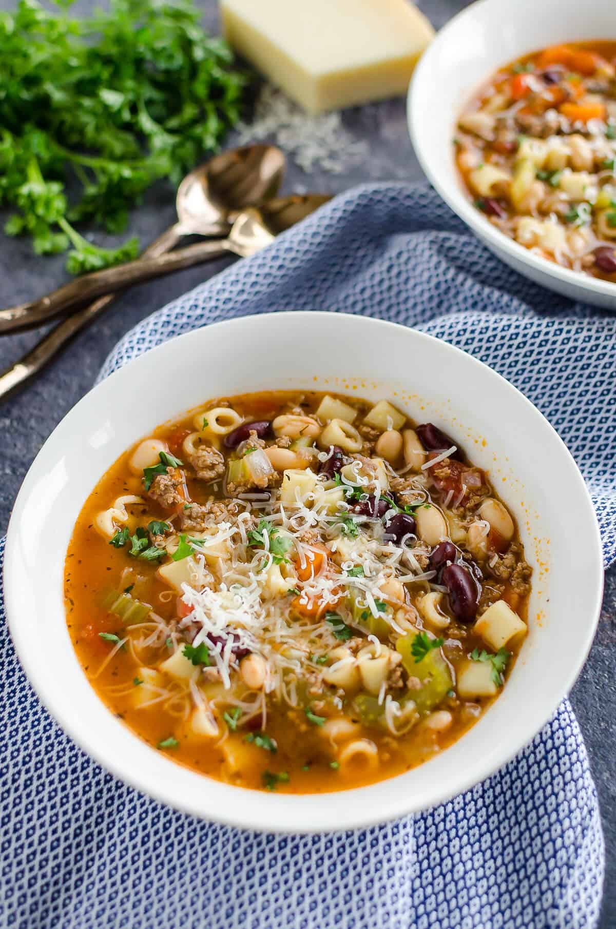 two white bowls of pasta fagioli soup garnished with parmesan cheese and parsley