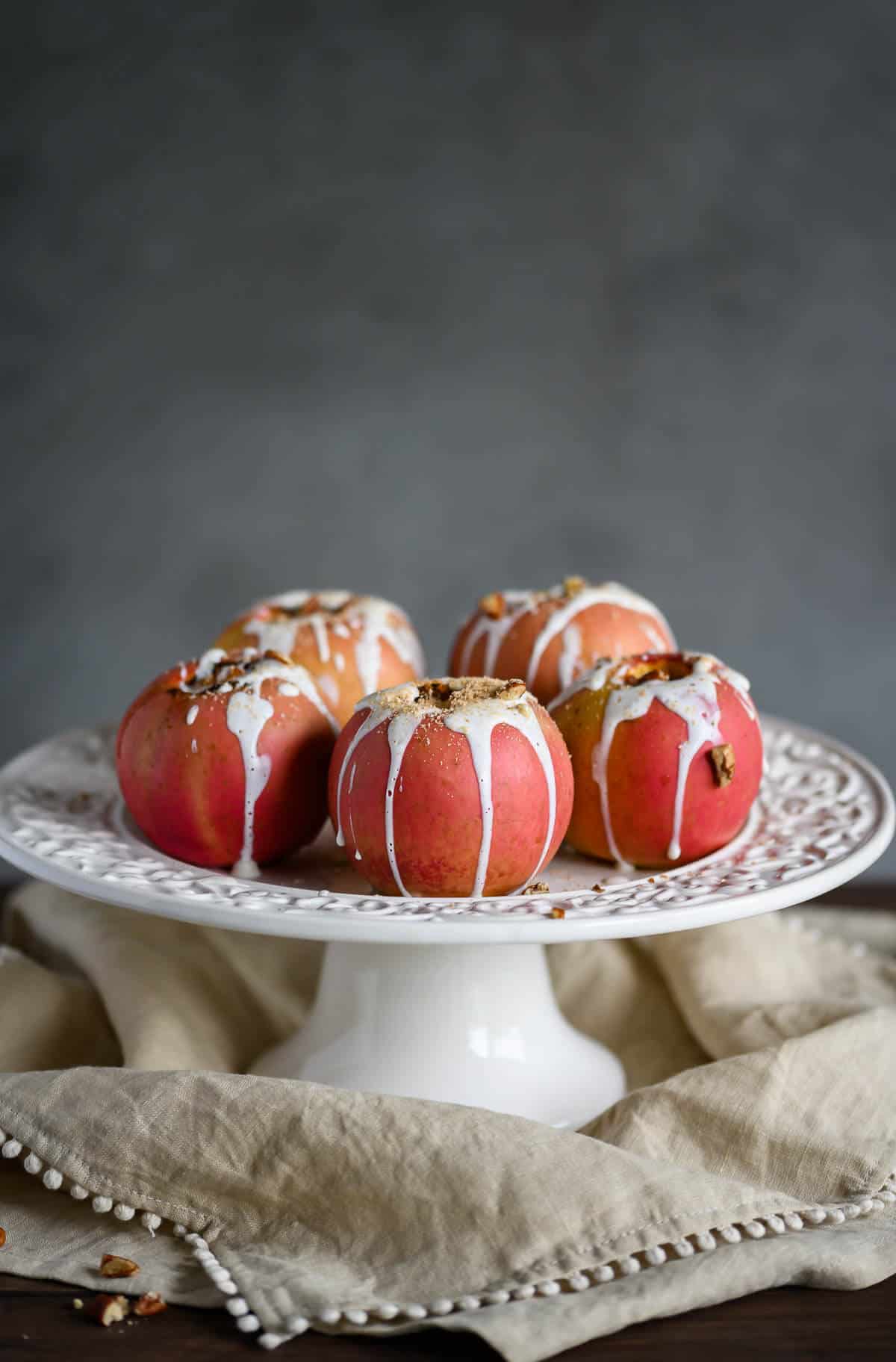 healthy baked apples drizzled with sweet yogurt sauce, pecans and cinnamon on a cake pedestal