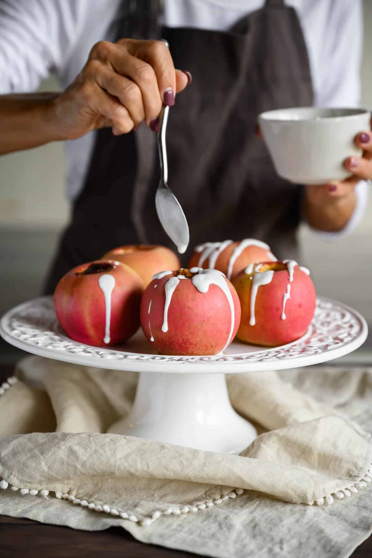 woman drizzling sweet yogurt sauce over baked apples on a white platter