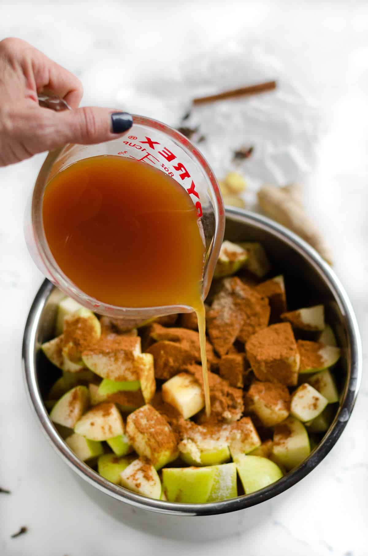 apple cider being poured over apples and spices in an instant pot for apple butter