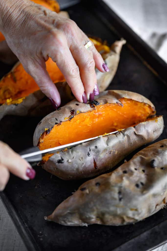 baked sweet potato being sliced lengthwise in half