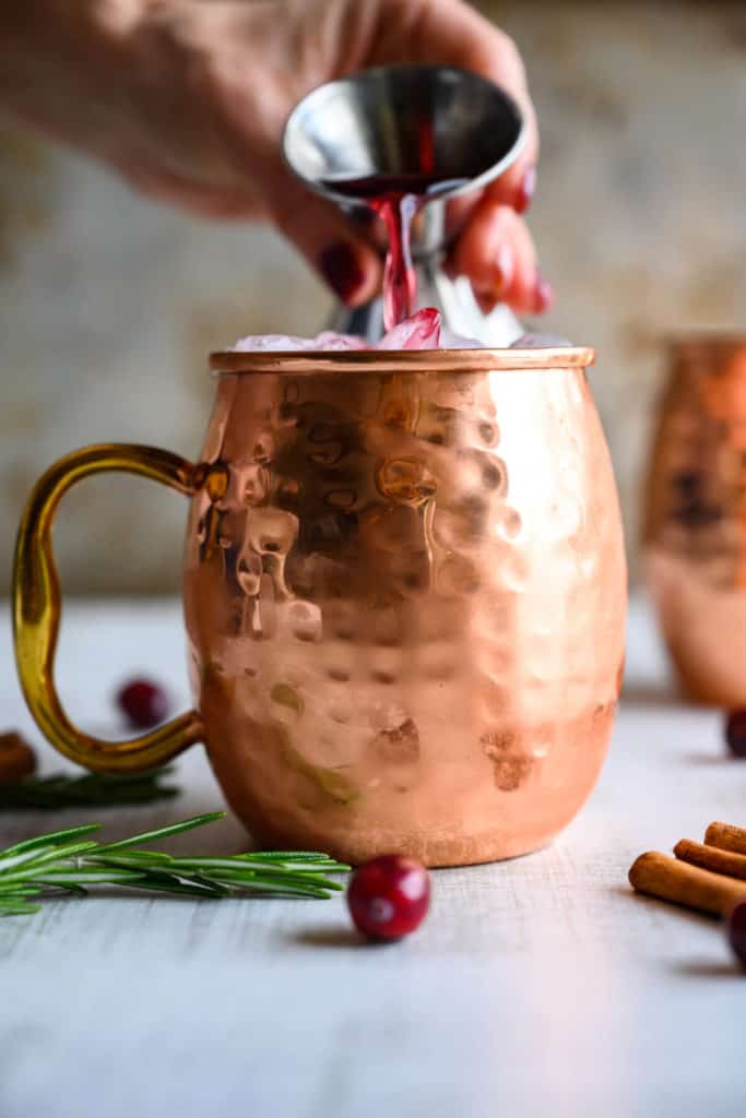 cranberry juice being poured into a copper mug over ice