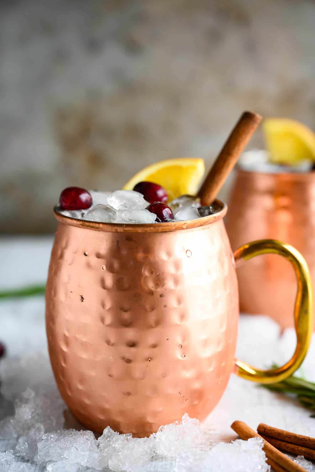 cold copper mug filled with non-alcoholic moscow mule, garnished with orange and cranberries