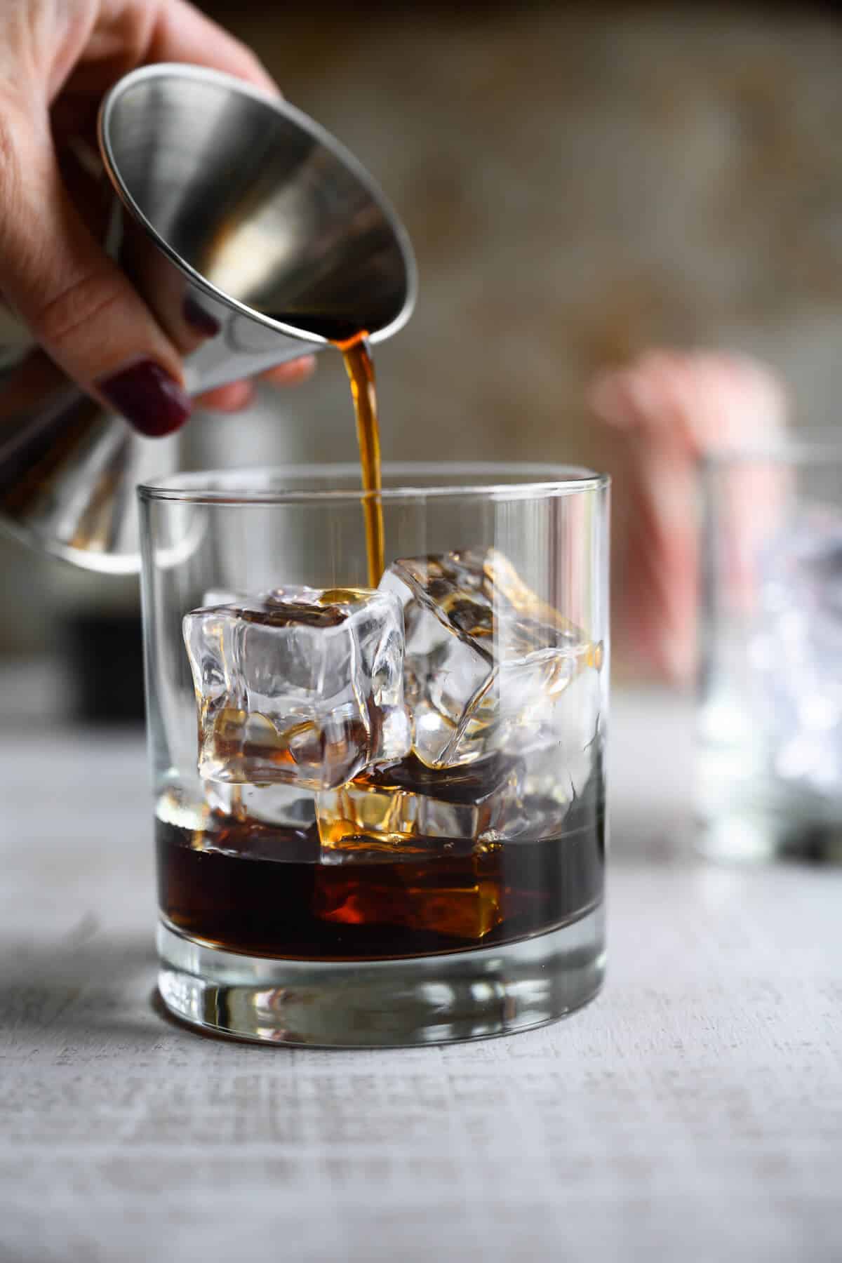 coffee being poured over ice from a jigger.