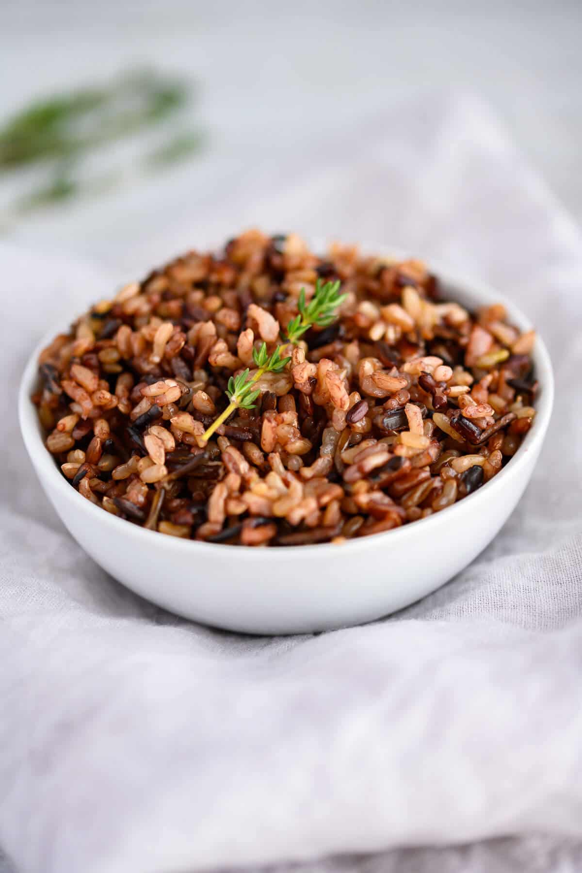 white bowl of cooked wild rice garnished with a sprig of thyme