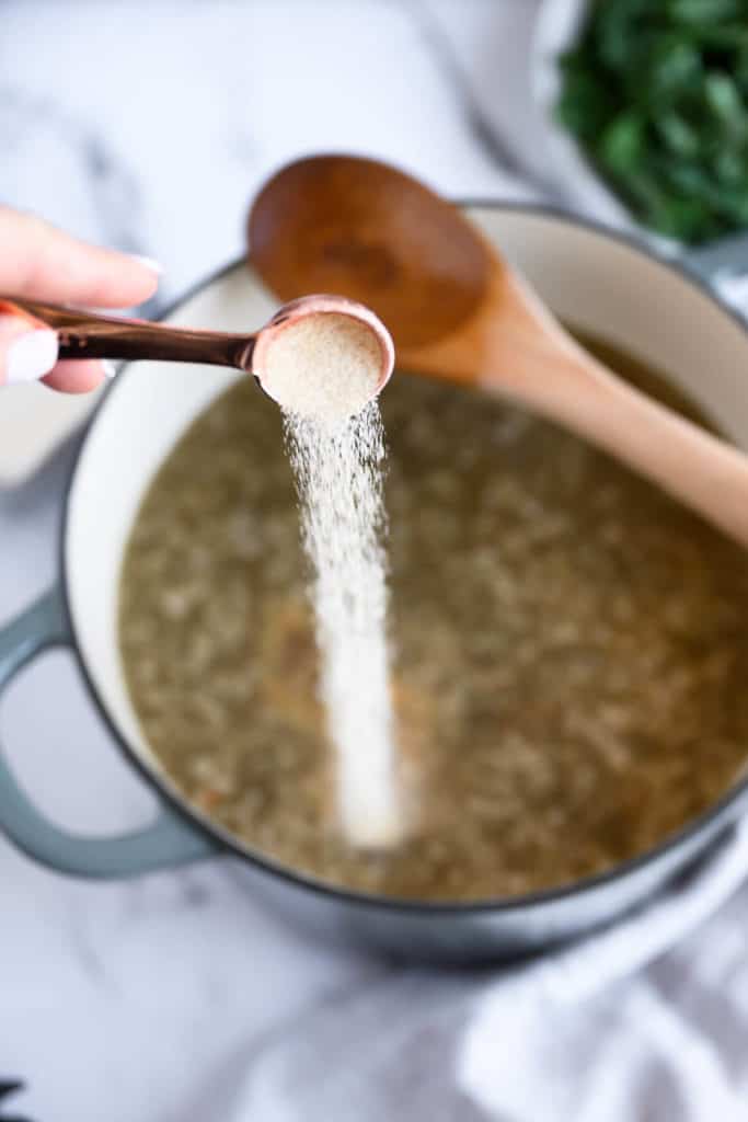 copper measuring spoon of garlic powder being poured into a pot of ground sausage