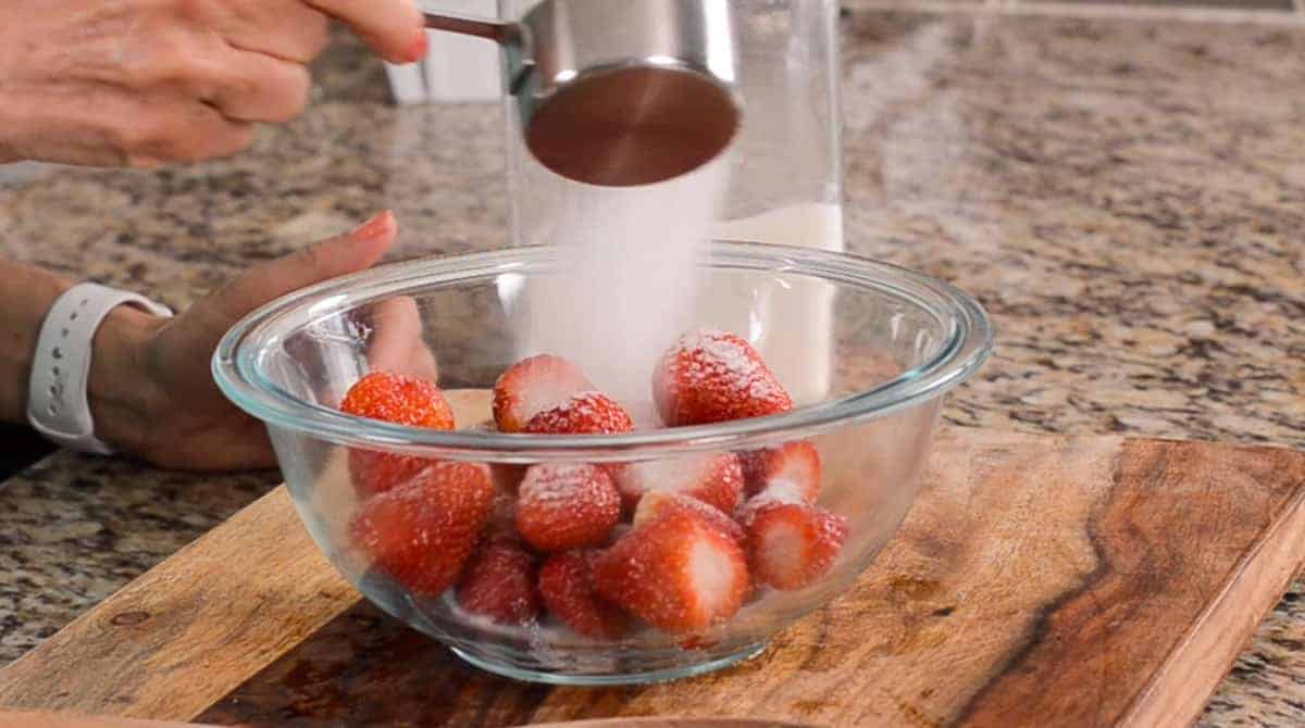 pouring sugar over a bowl of fresh strawberries