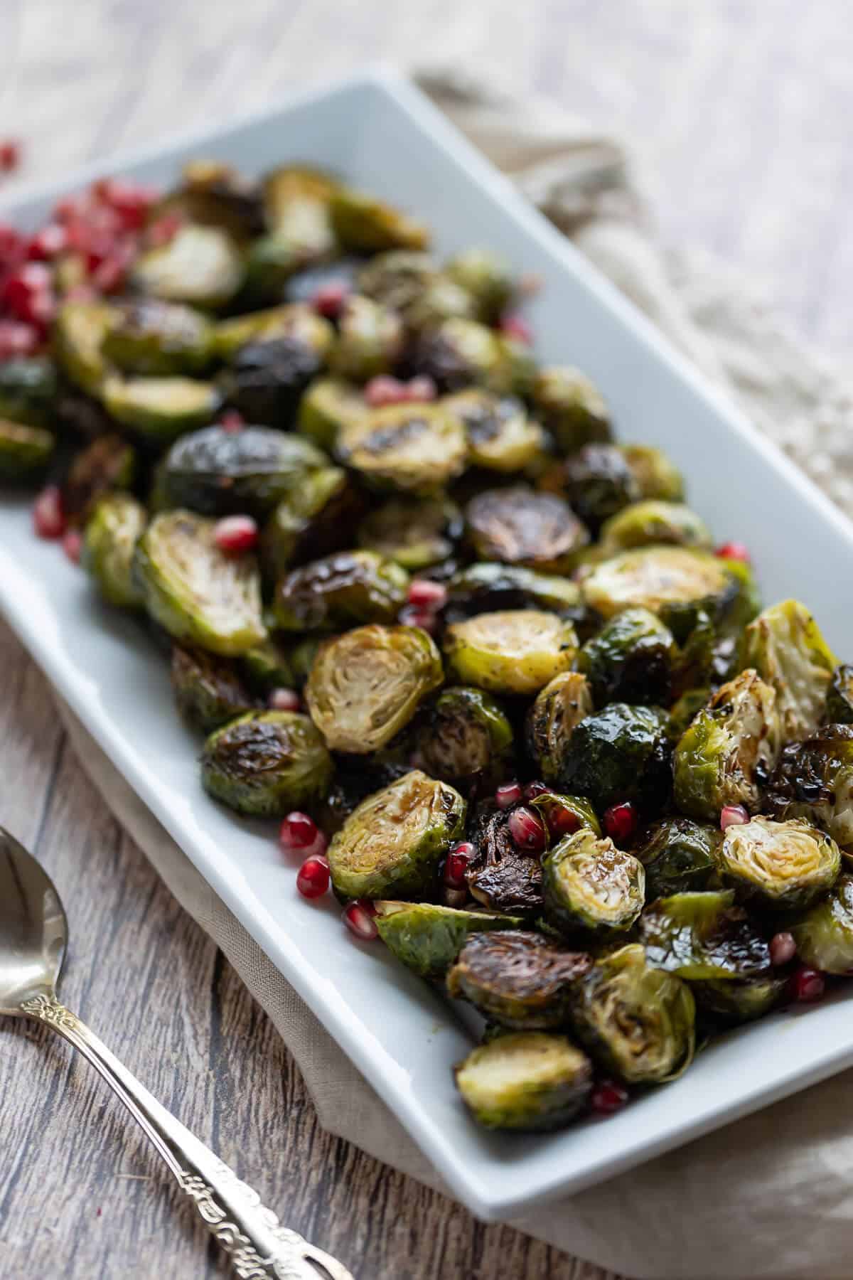 Platter of roasted brussels sprouts garnished with pomegranate seeds.