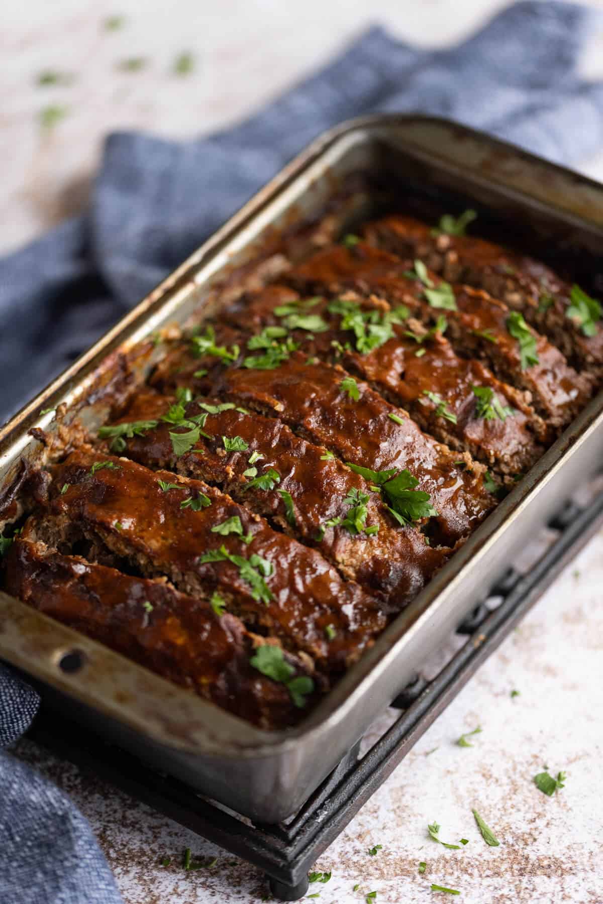 cooked meatloaf in a loaf pan that has been glazed with bbq sauce and garnished with fresh parsley