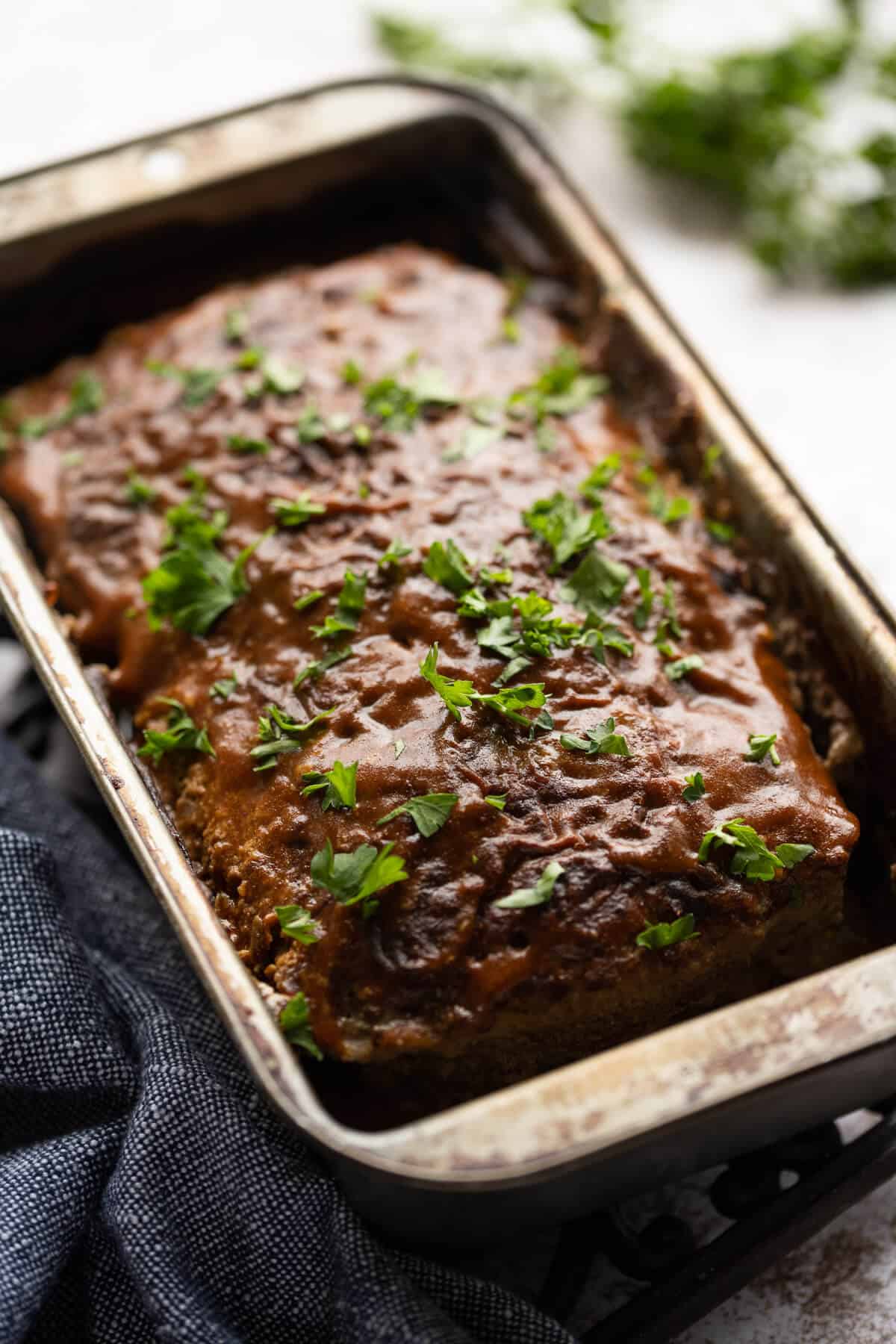 cooked meatloaf glazed with bbq sauce and garnished with parsley in a loaf pan