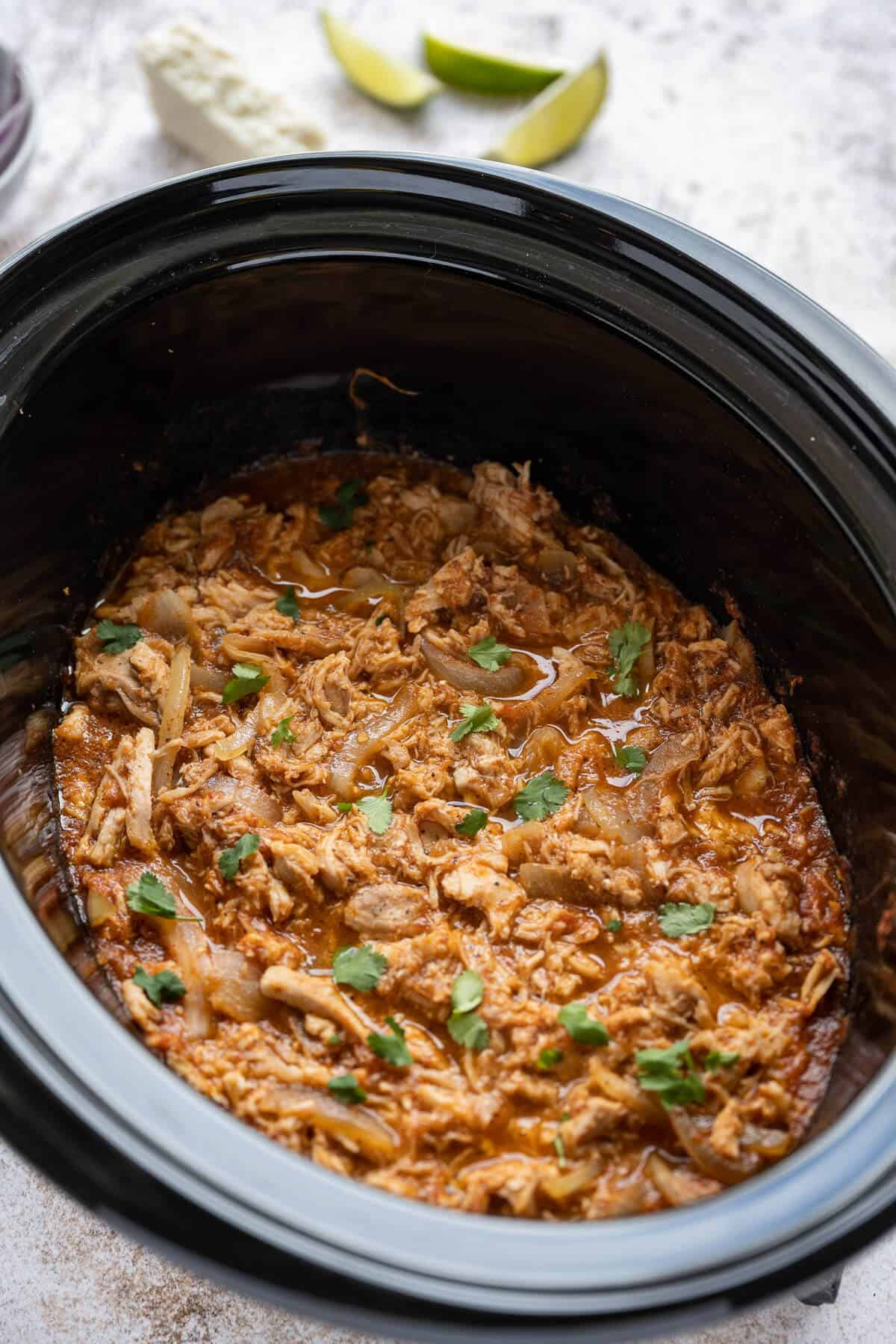 cooked chicken tinga simmering in sauce in a crockpot garnished with cilantro
