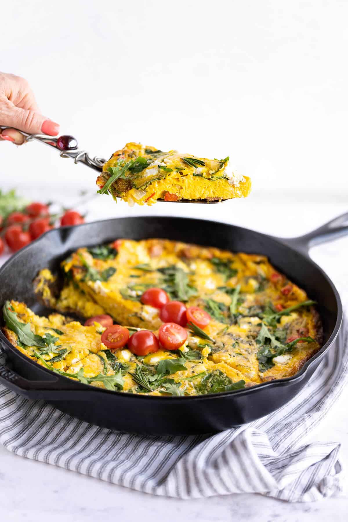 slice of frittata on a spatula being held above the whole frittata in a cast iron pan