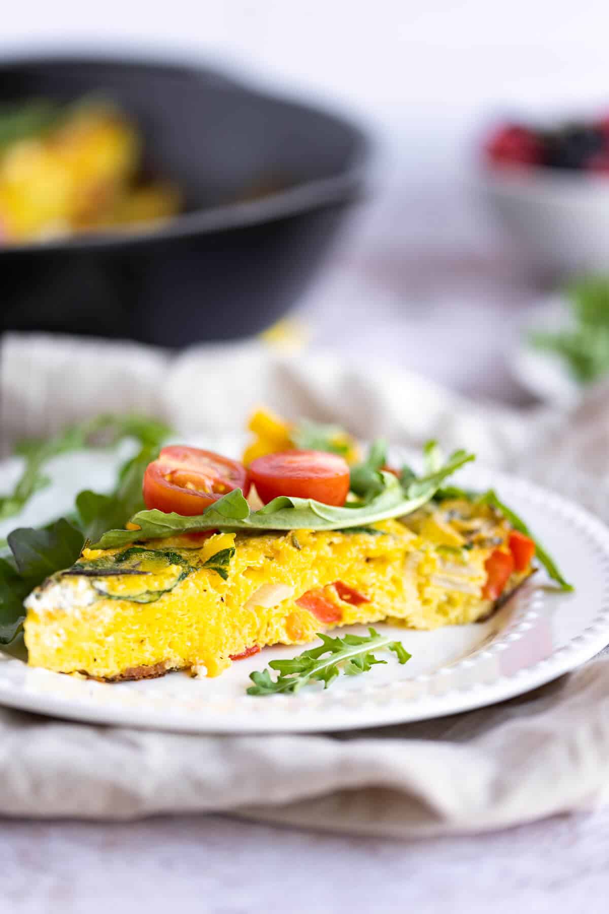 side view of a fluffy egg frittata topped with arugula and tomatoes