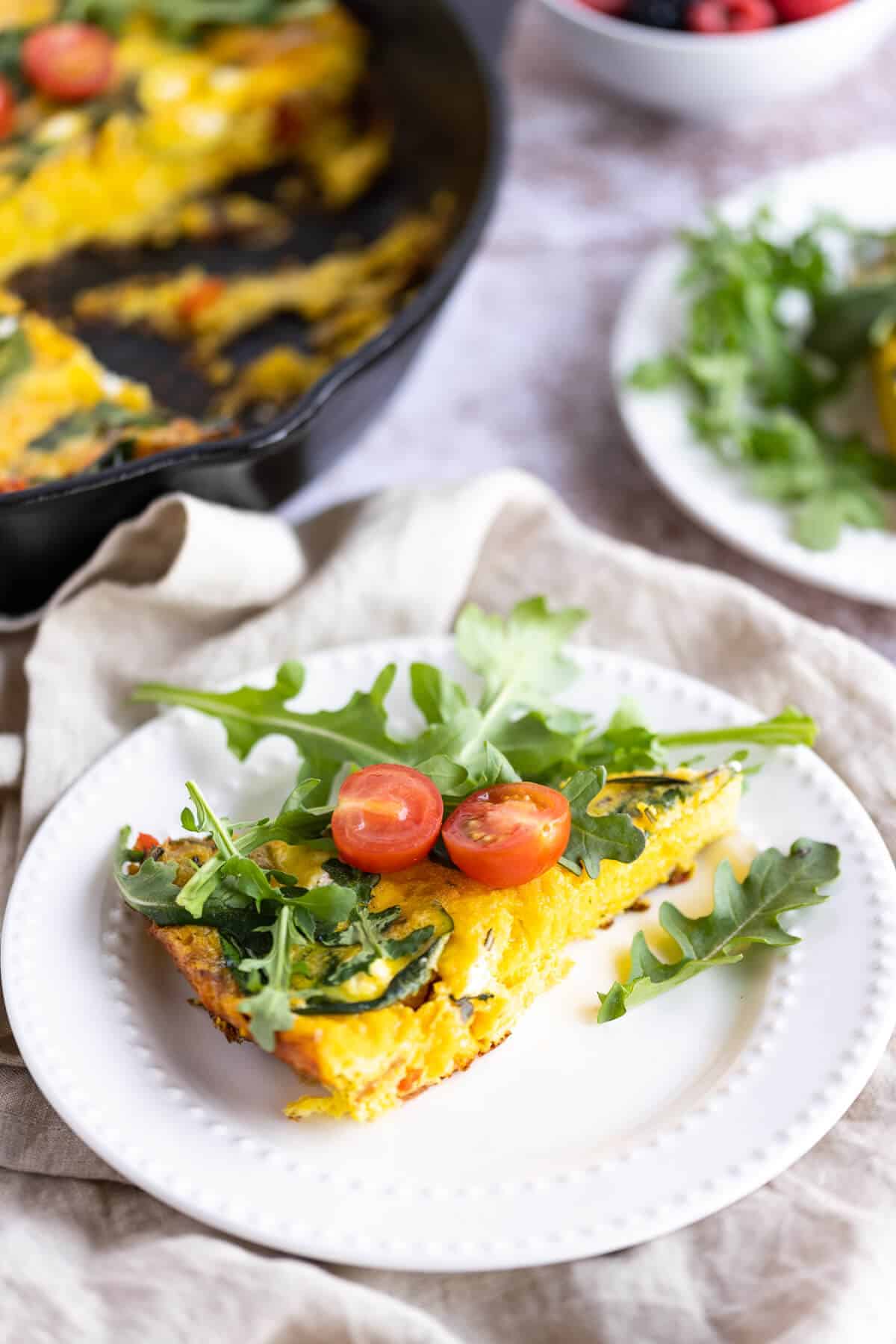 slice of a frittata on a white plate garnished with arugula