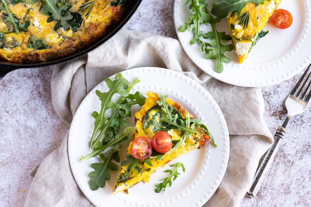 2 white plates with a slice of fluffy egg frittata on each garnished with arugula and tomatoes