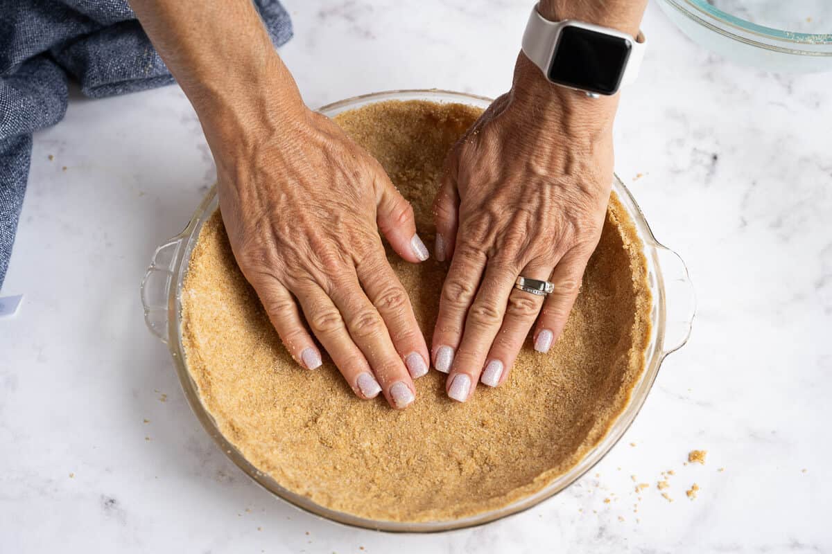 graham cracker crumb crust being pressed into a pie plate