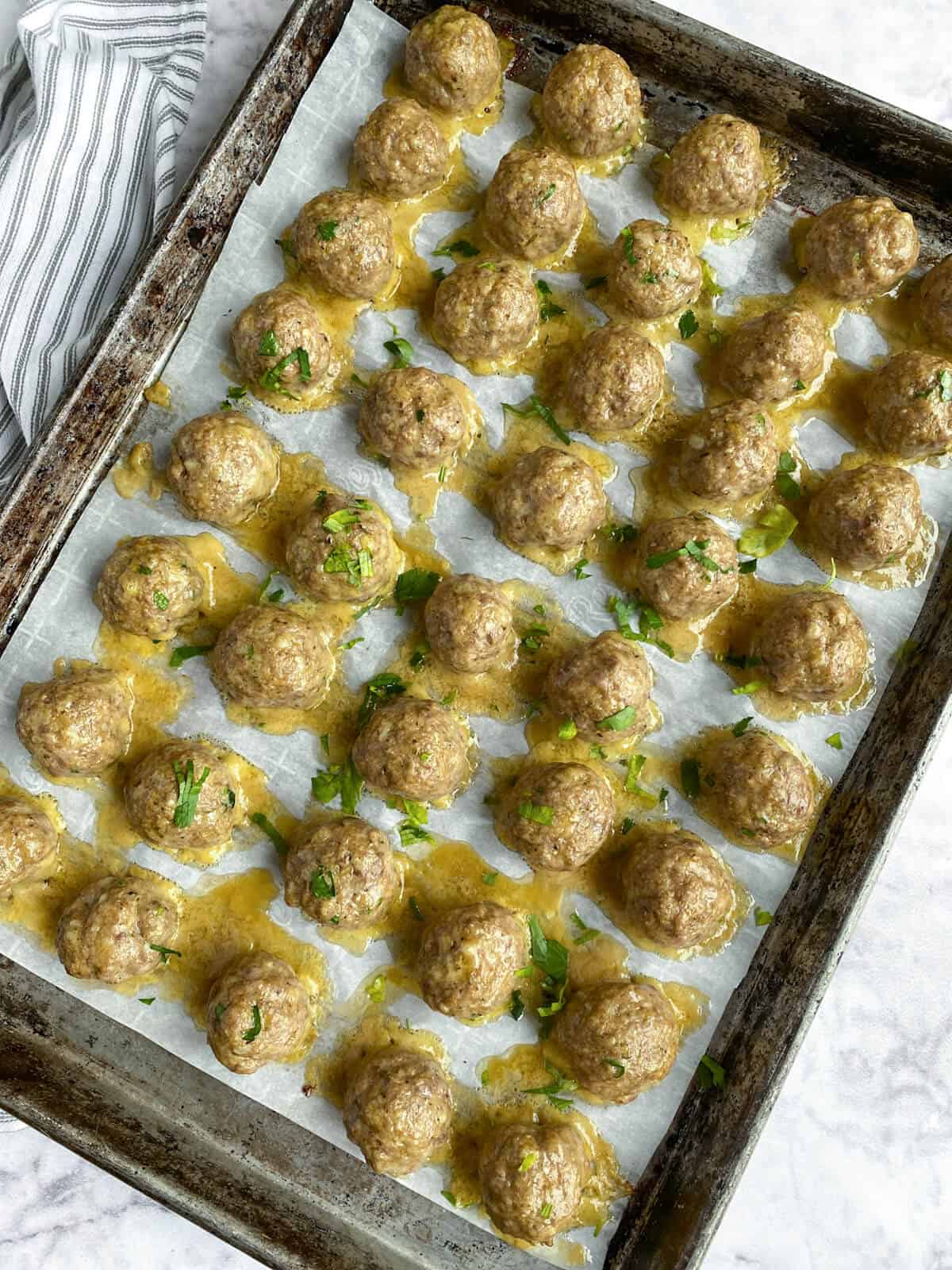 cooked meatballs on a parchment lined rimmed baking sheet
