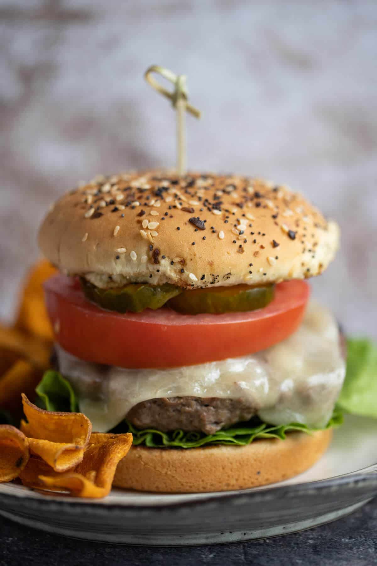 hamburger with cheese, lettuce, tomato and pickle on an onion bun