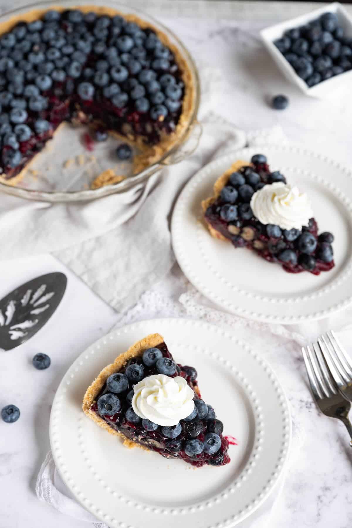 two slices of blueberry pie plated next to whole pie