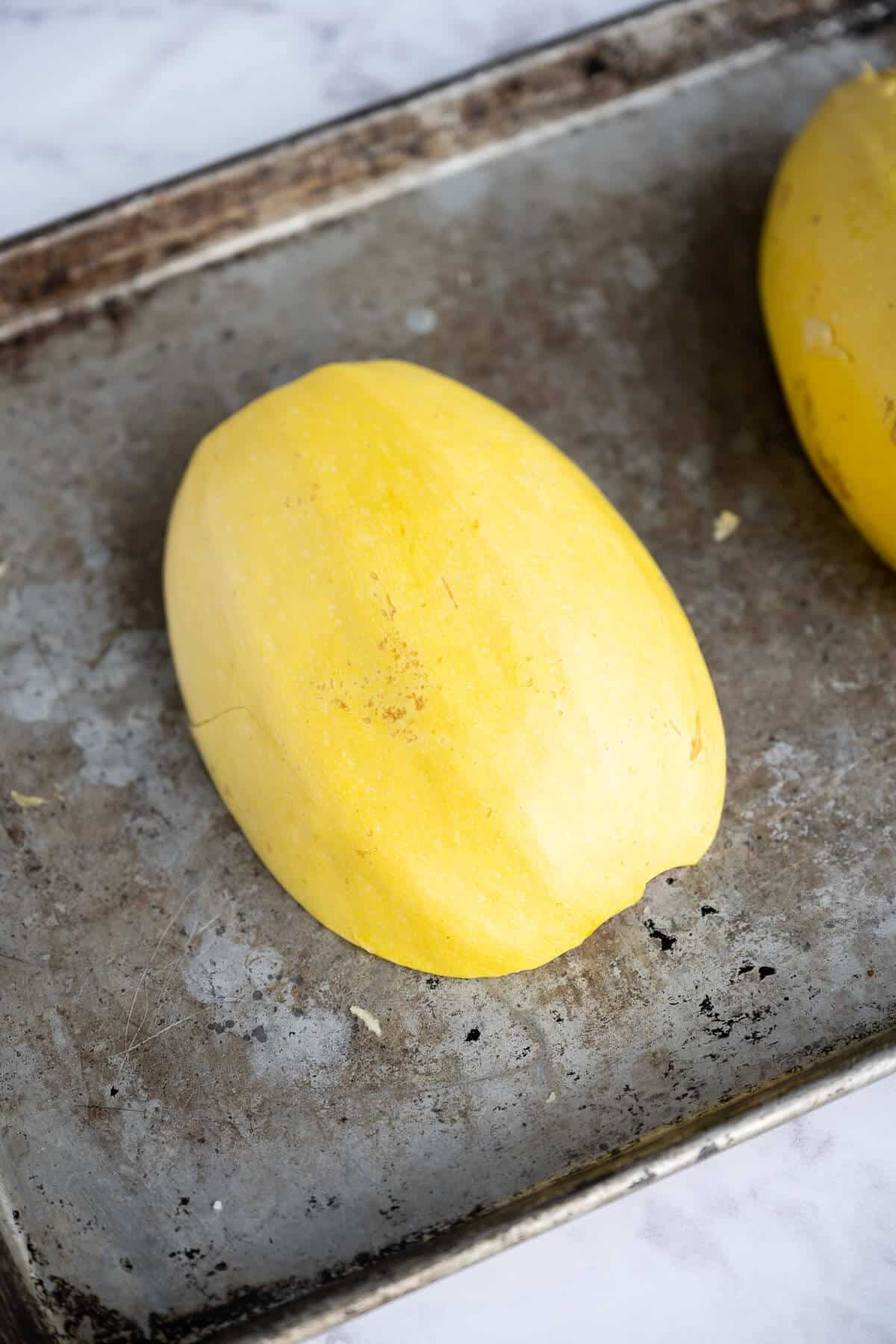spaghetti squash sliced in half lengthwise cut side down on rimmed baking sheet.