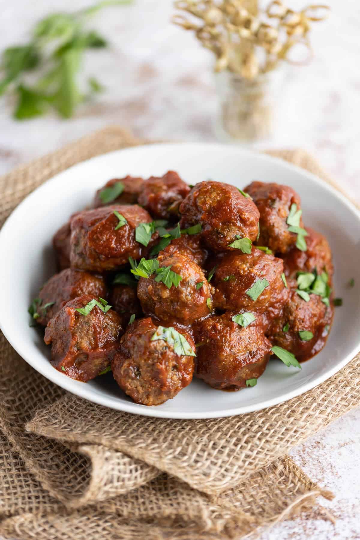 BBQ party meatballs in a white serving dish garnished with parsley, alongside toothpicks for serving.