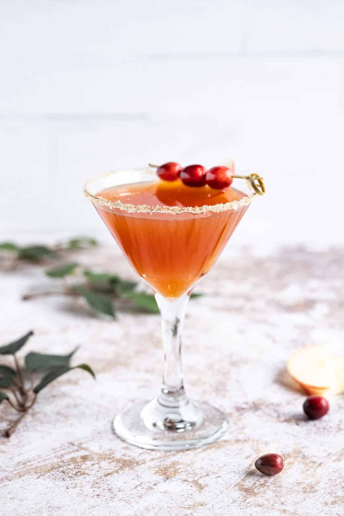 apple cider mocktail in a martini glass rimmed in sugar and garnished with fresh cranberries