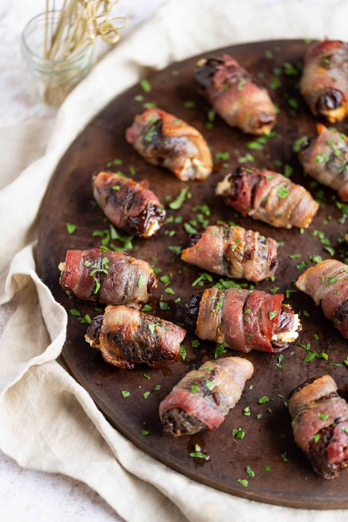 Goat cheese stuffed dates, wrapped in bacon, on a round serving platter.