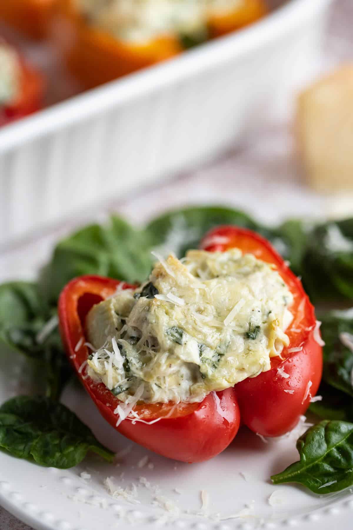Red bell pepper half full of chicken, spinach, and artichoke dip on a bed of spinach.