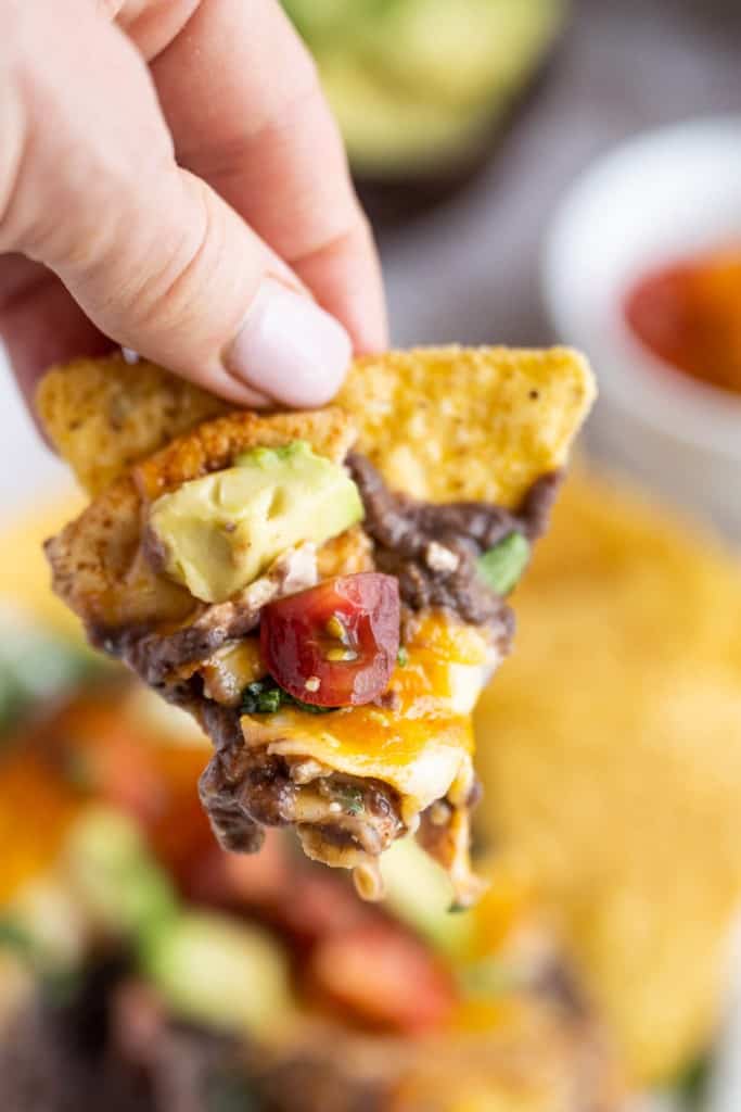 A hand holding a tortilla chip with the black bean dip on it.