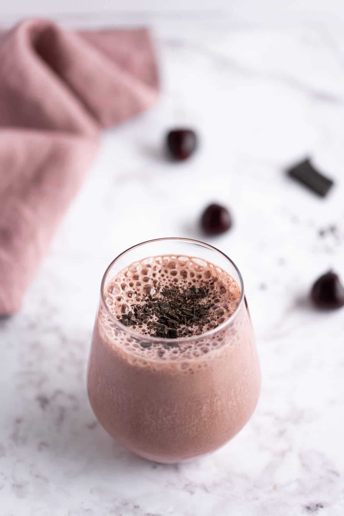 Full glass of Chocolate Cherry Smoothie with a frothy top and garnished with shaved dark chocolate.