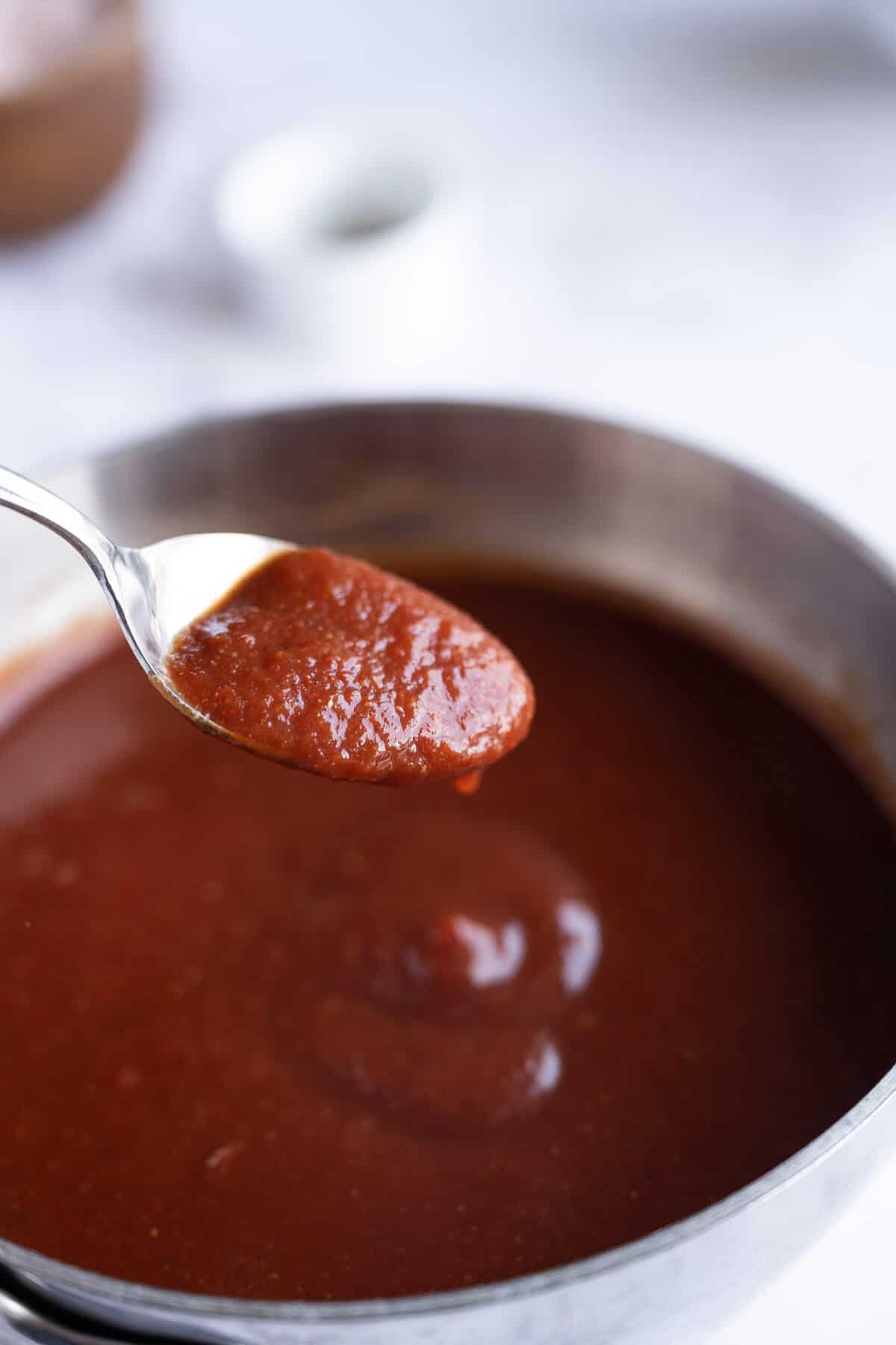A spoonful of homemade keto barbecue sauce being held up above the pan of simmering sauce.