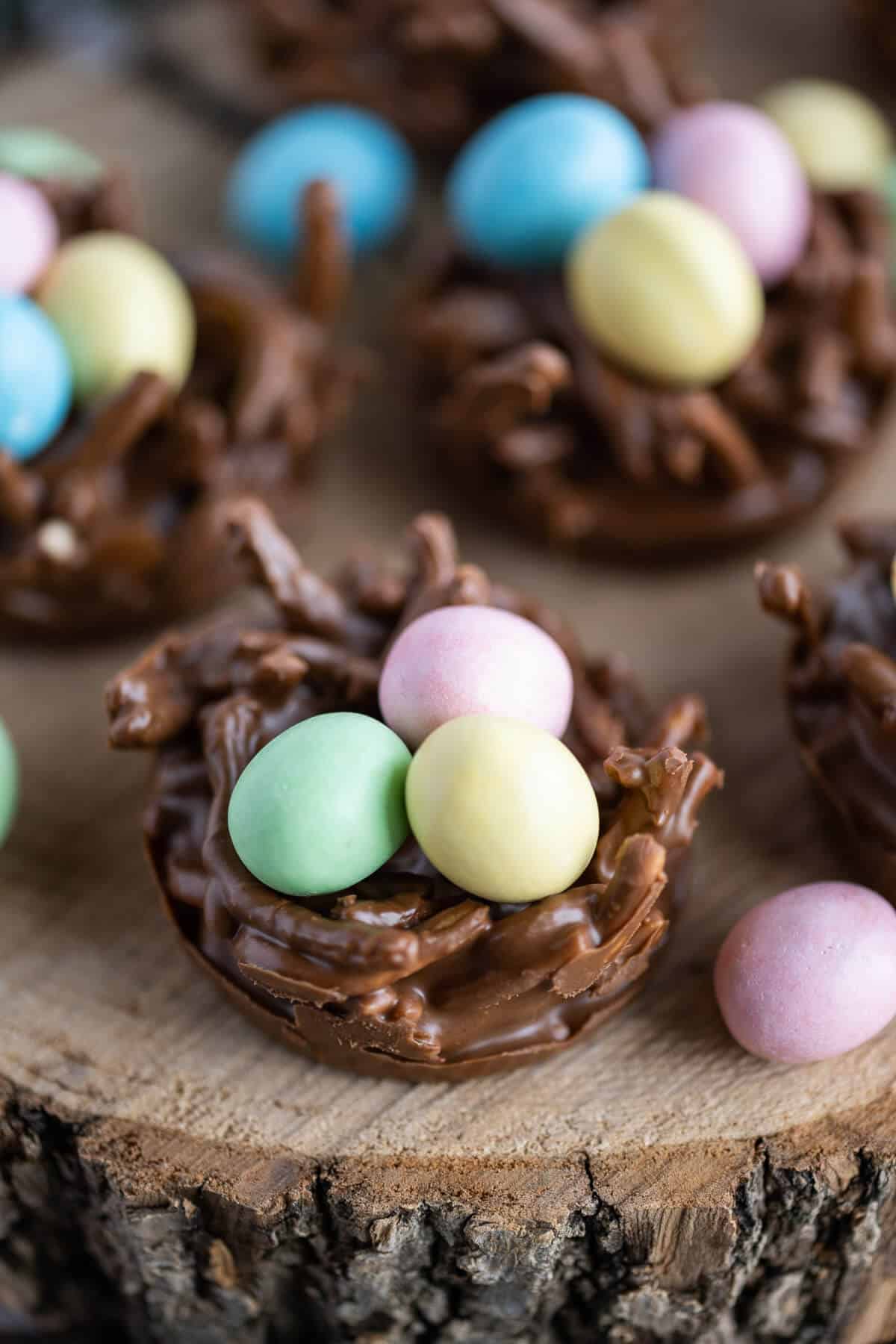 No Bake Bird Nest Cookies made out of chocolate and chow mein noodles, filled with pink, yellow, green, and blue candy eggs.