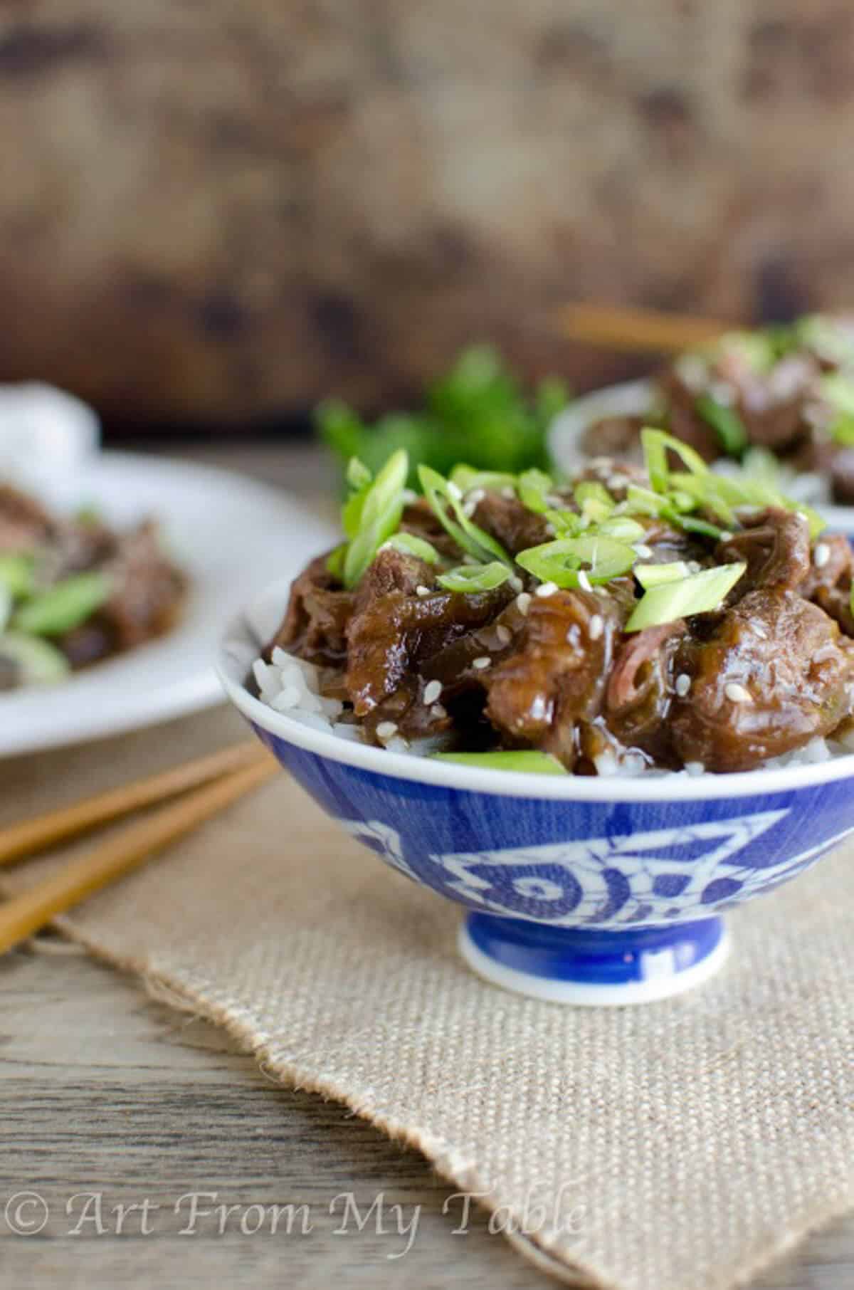 Bowl of Mongolian Beef, garnished with green onions and sesame seeds on top of a bed of white rice.