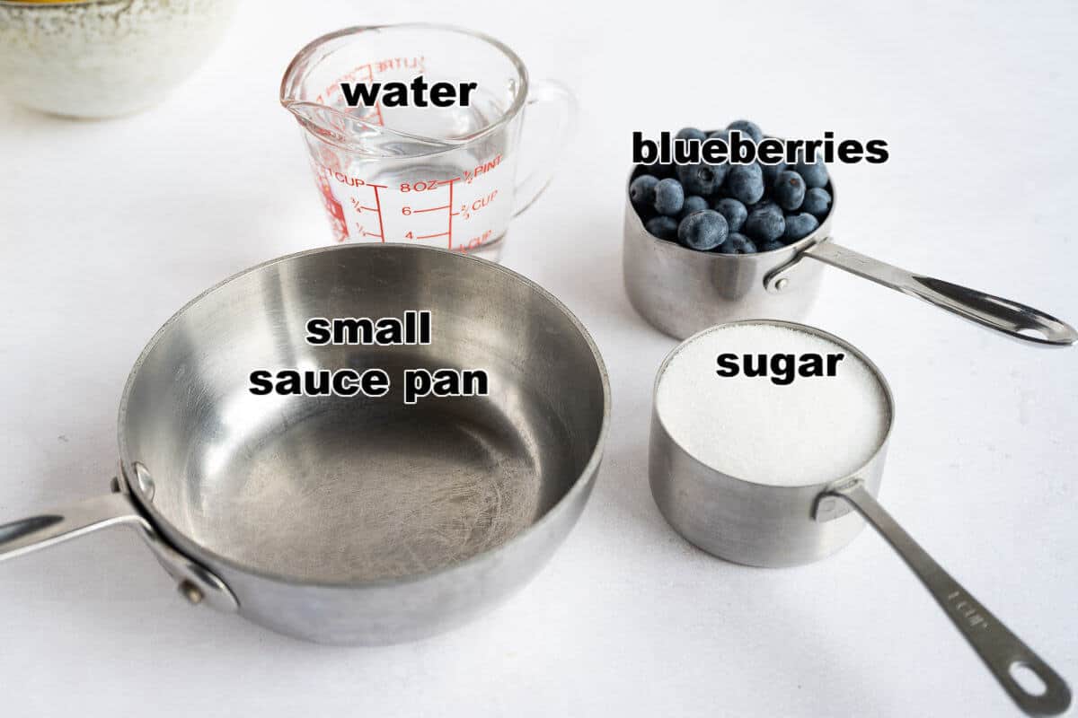 3 one-cup measuring cups: one with water, one with fresh blueberries, one with sugar. All next to a small saucepan.