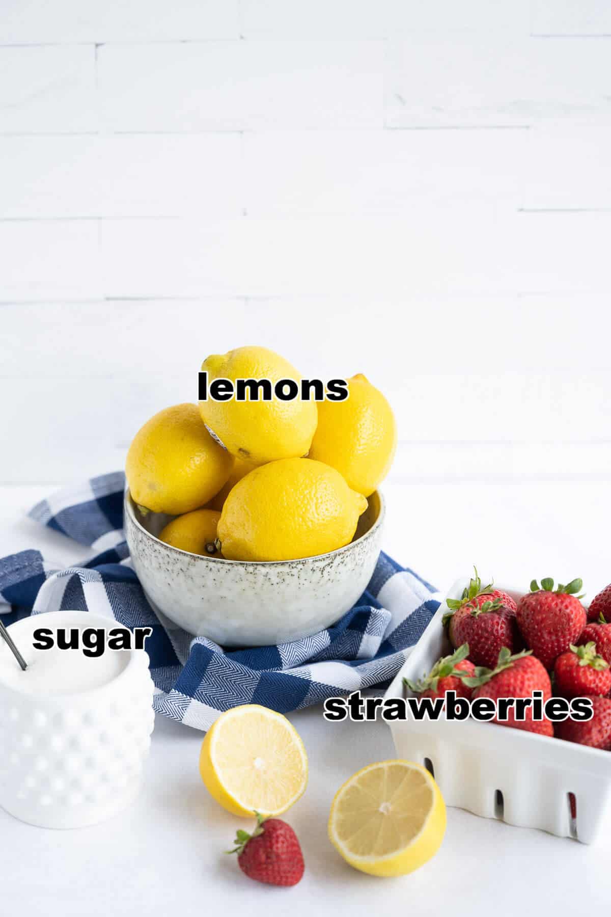 Bowl full of lemons sitting next to a container of sugar and a quart of fresh strawberries.