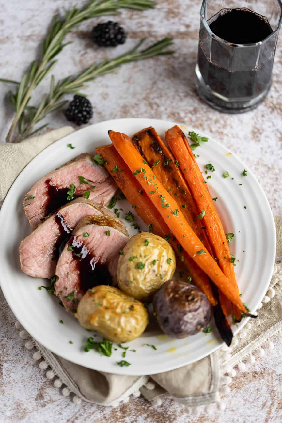 A few slices of pork tenderloin, drizzled with blackberry sauce, on a white plate with roasted carrots and potatoes.