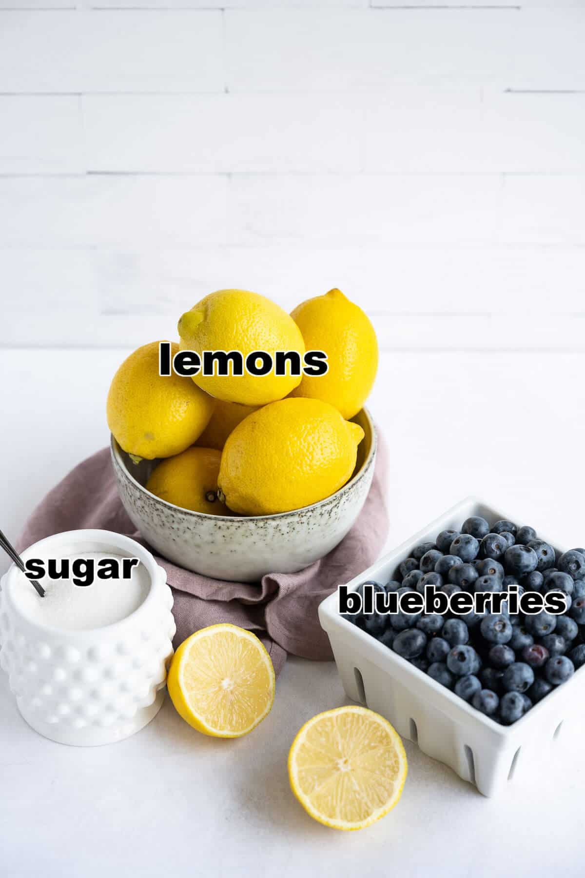 A bowl of Lemons, container of blueberries, and a jar of sugar.