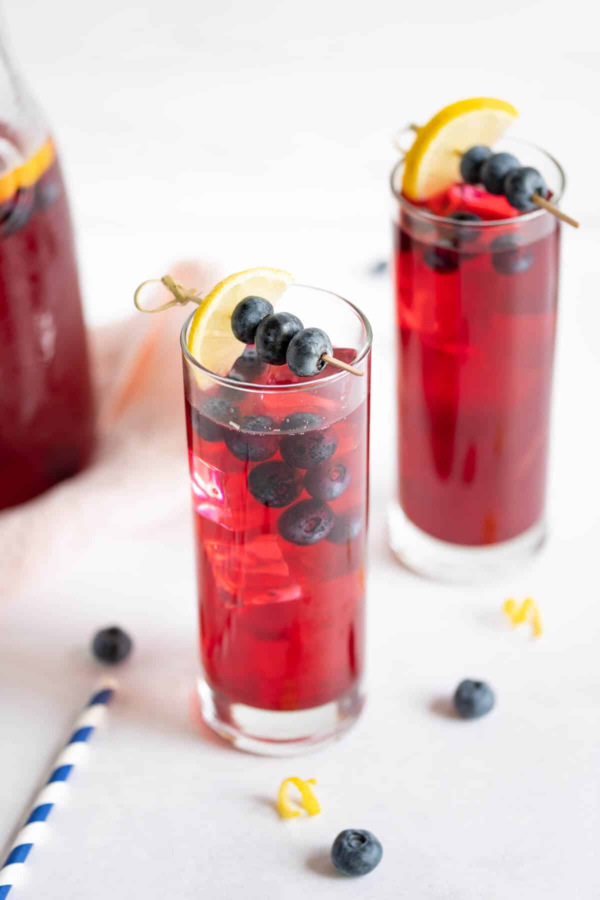 2 glasses of blueberry lemonade garnished with sliced lemon and fresh blueberries.