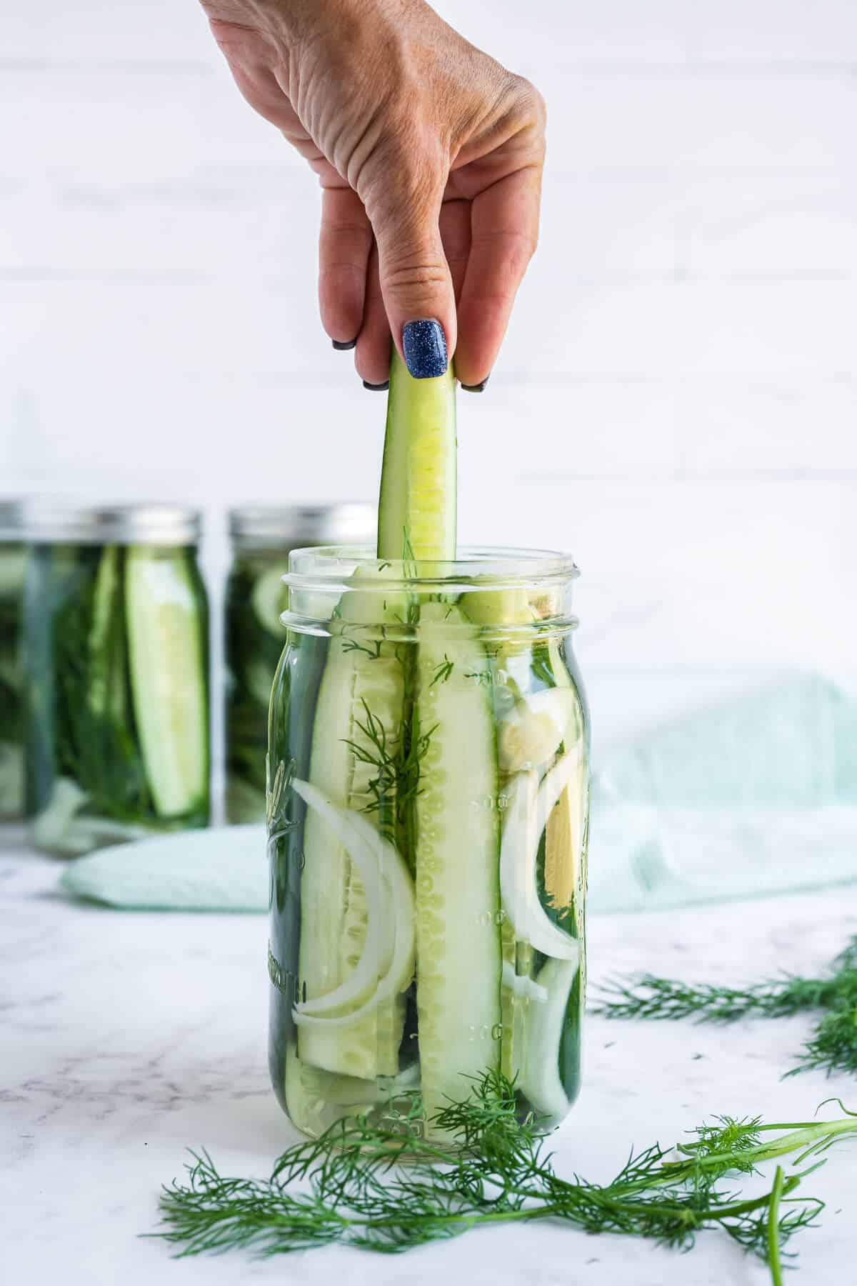 Spear shaped pickle being pulled out of a mason jar.
