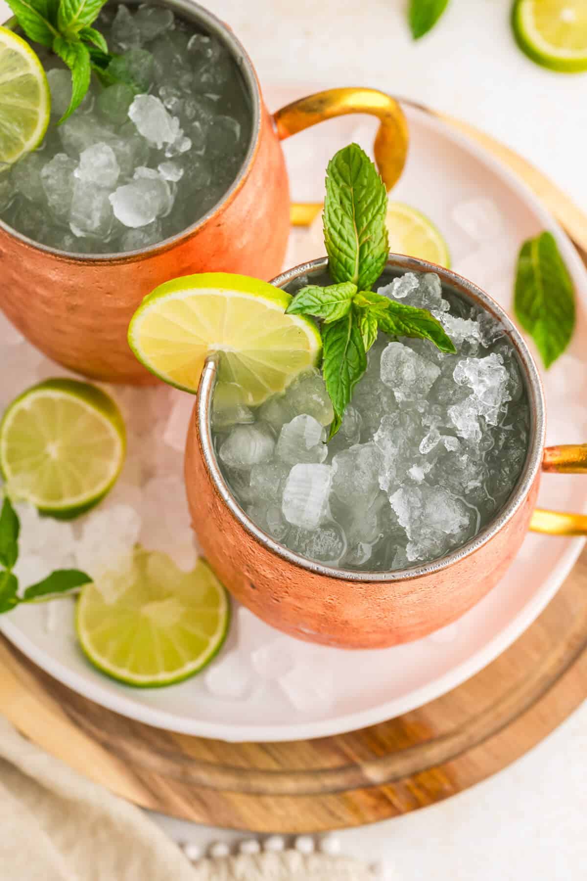 Top view of 2 Moscow Mules in copper mugs garnished with lime slices and fresh mint. Mugs are on a round serving platter.