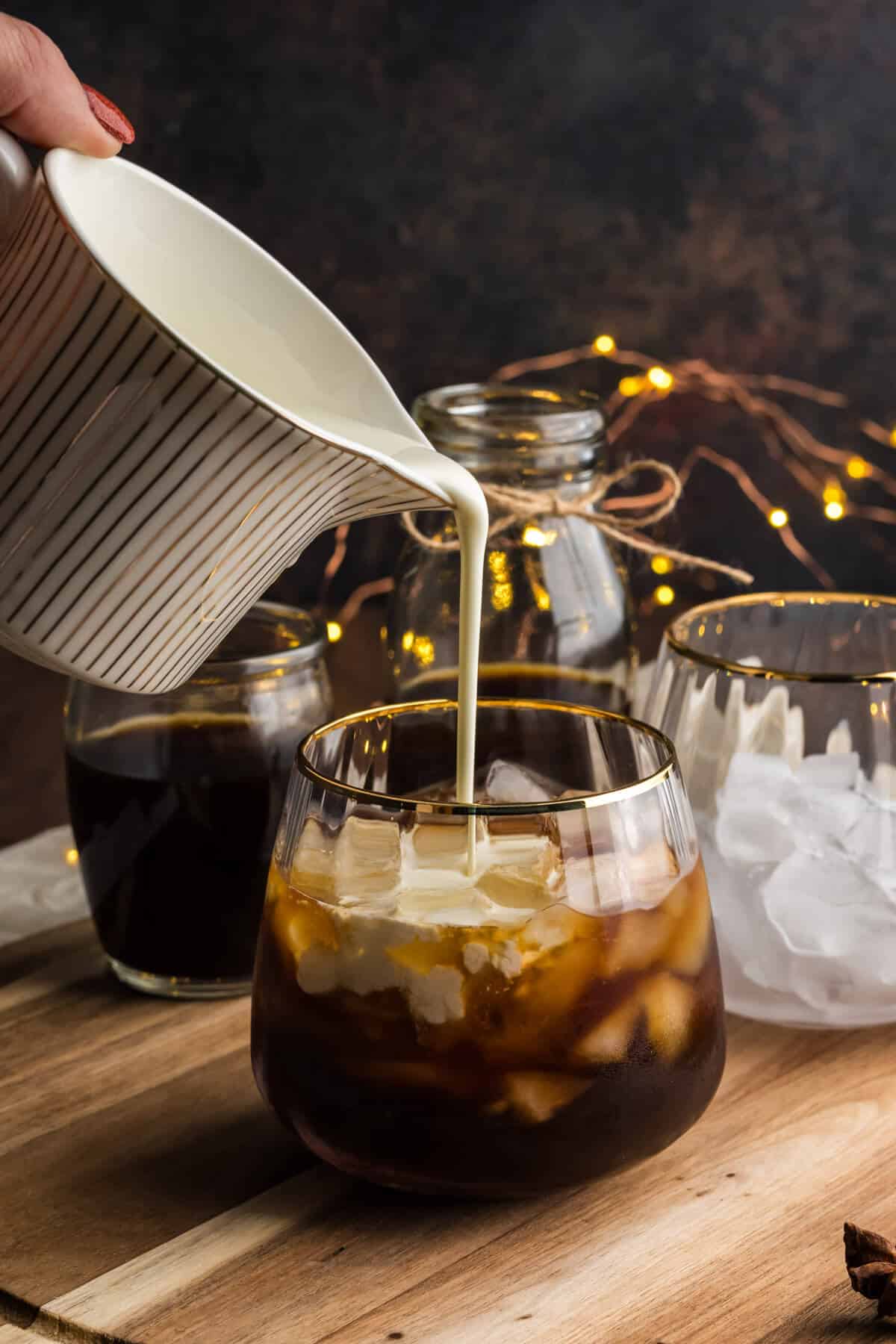 Heavy cream being poured into a cocktail glass containing coffee and gingerbread syrup.
