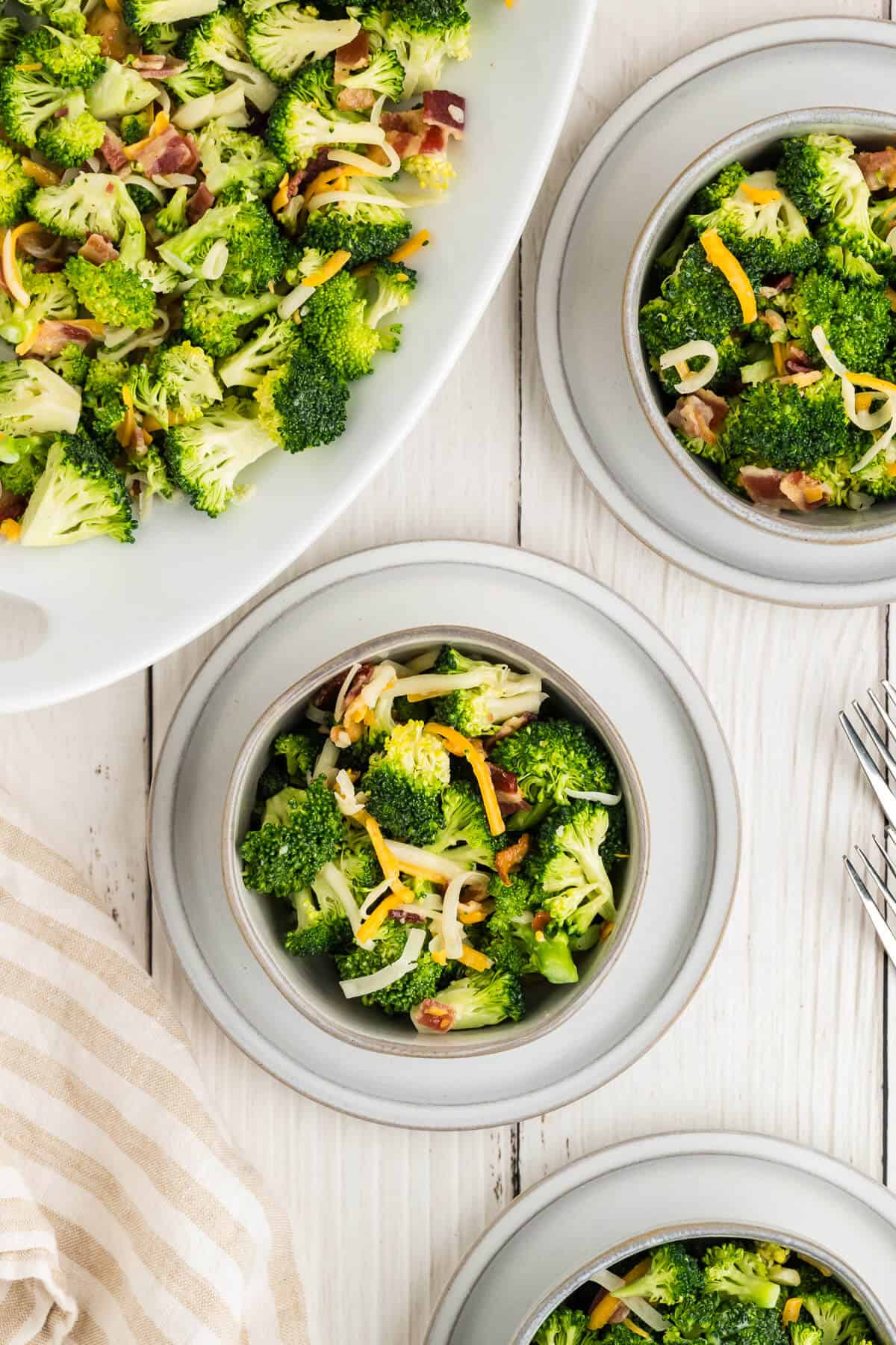 Platter of Broccoli Salad and small bowls of it next to the platter. The broccoli salad has shredded cheddar and Mozzarella cheese in it and bacon.