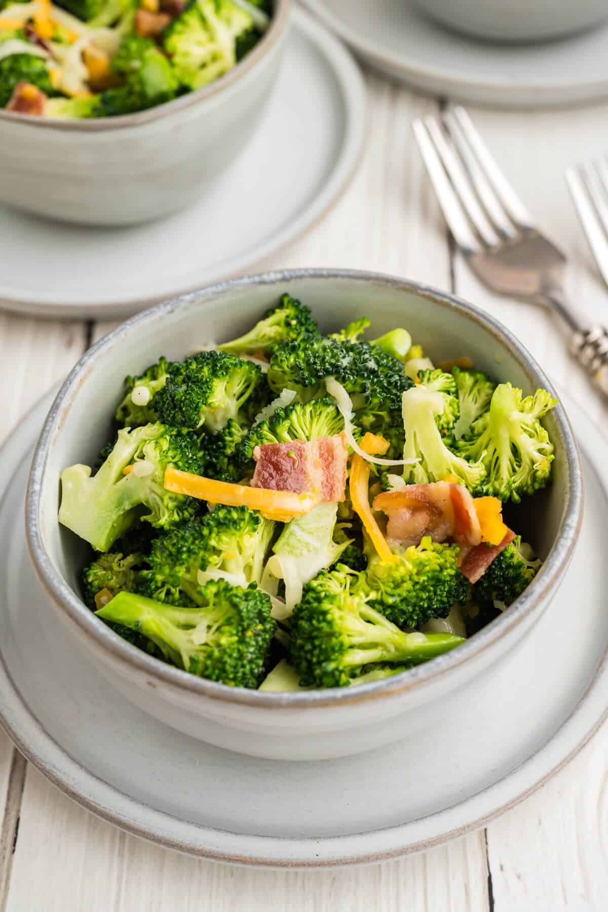 A bowl of broccoli salad with more bowls in the back ground and a couple of forks.