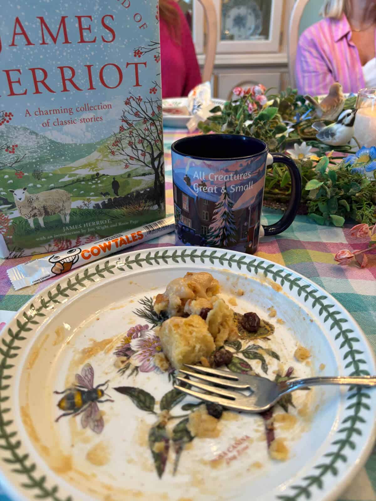 A plate of mostly eaten bread pudding with an All Creatures Great and Small coffee mug and the book "The Wonderful World of James Herriot"