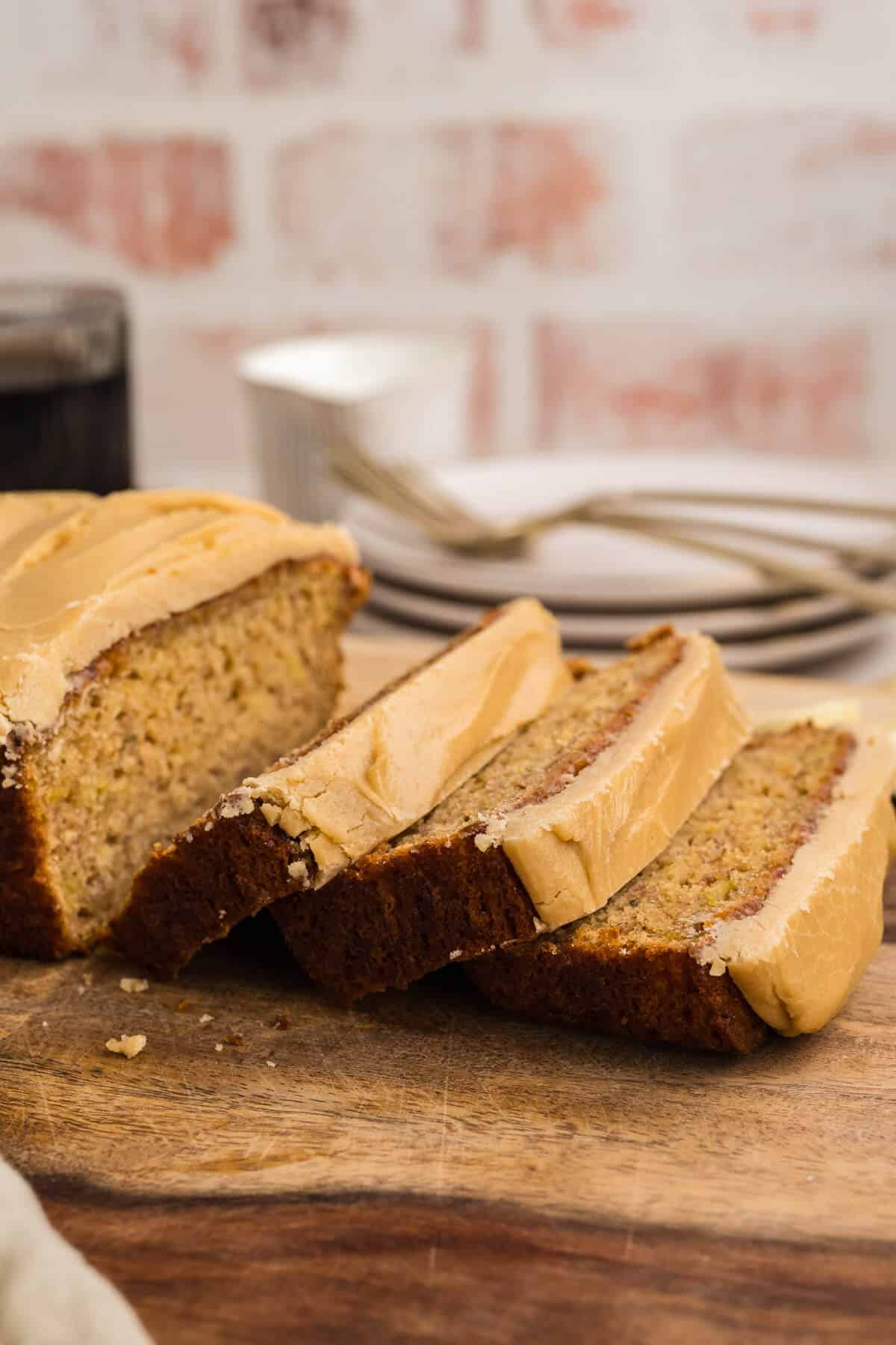 A loaf of banana bread with caramel icing, with three slices laying down on a cutting board next to the loaf itself.