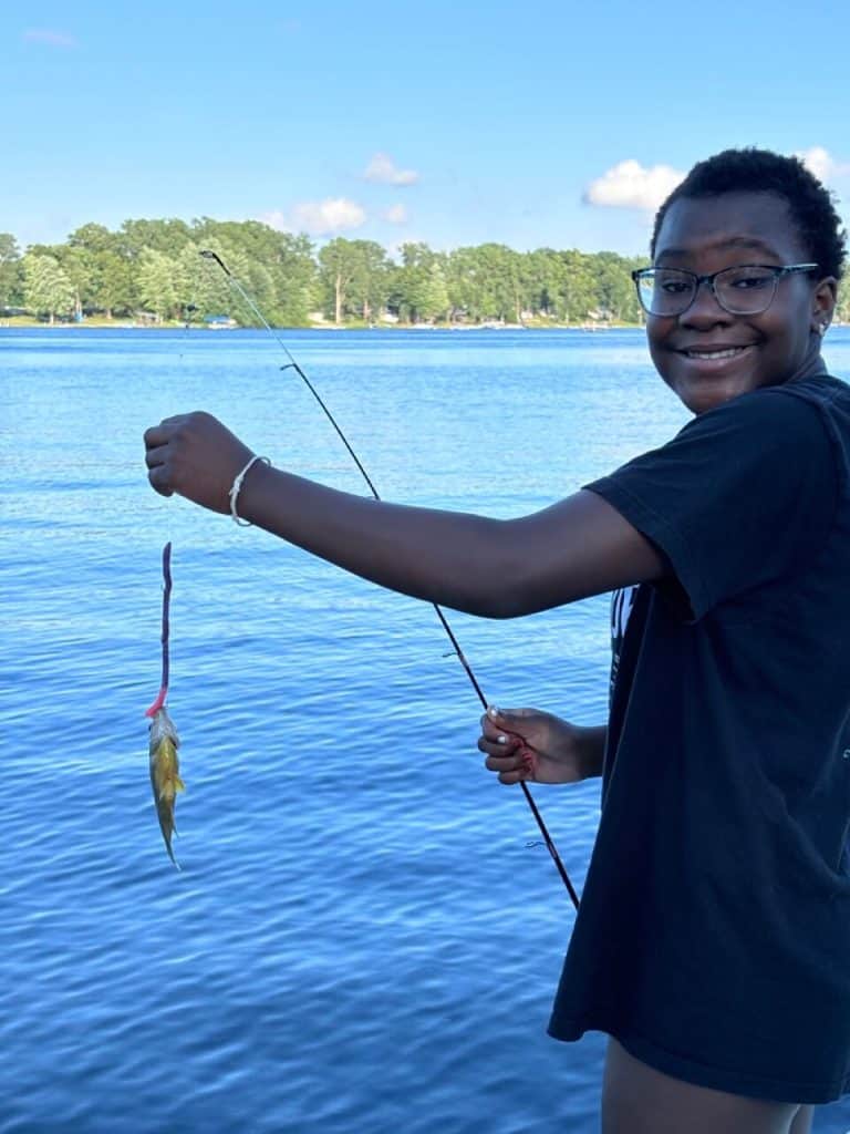 Girl holding a fish on a fishing pole with lake in the background.