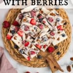 Frozen Yogurt Bark with berries and pecans on a round wooden board, garnished with some fresh berries on top and scattered around. Text overlay reads: Yogurt Bark with Berries.