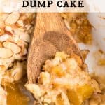 A scoop of peach dump cake on a wooden spoon laying in the corner of a 9x13 white casserole dish. Text overlay reads: Peach Dump Cake.