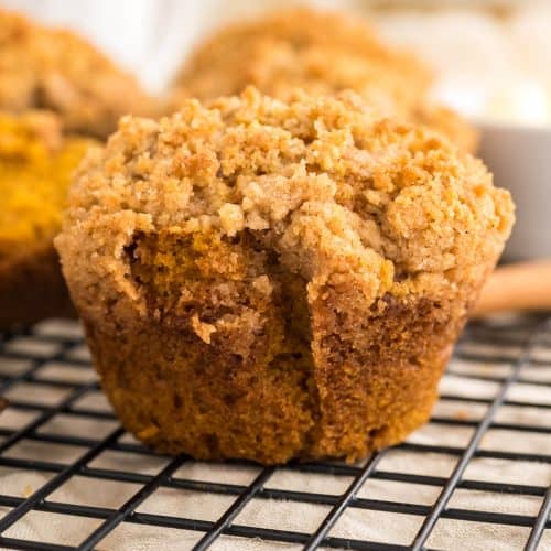 Pumpkin Muffin with Streusel topping on a. baking rack with more muffins blurred out behind it.