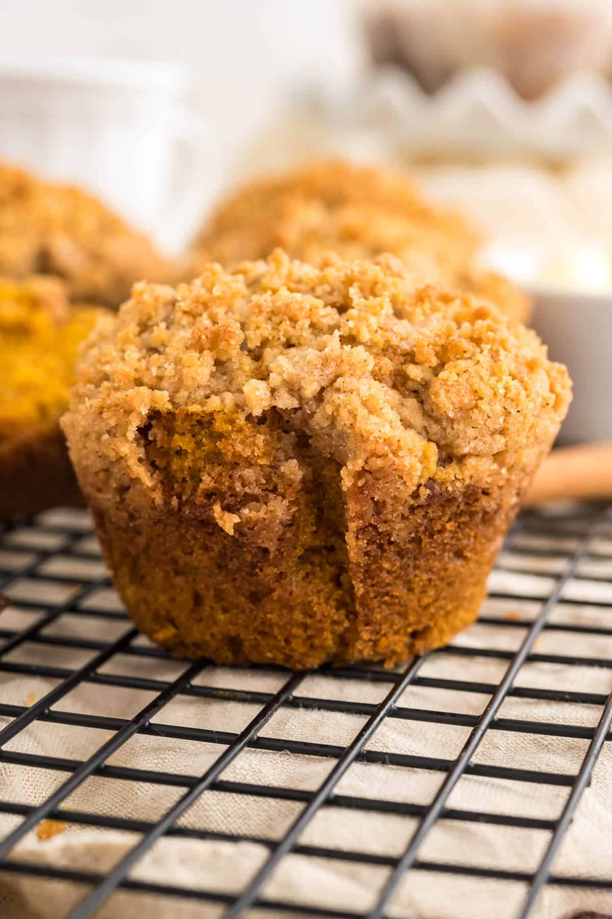 Pumpkin Muffin with Streusel topping on a. baking rack with more muffins blurred out behind it.